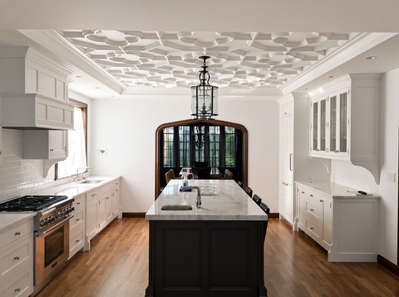 Custom kitchen with white cabinetry, a dark wood island, an ornamental coffered ceiling, and a wood-trimmed archway